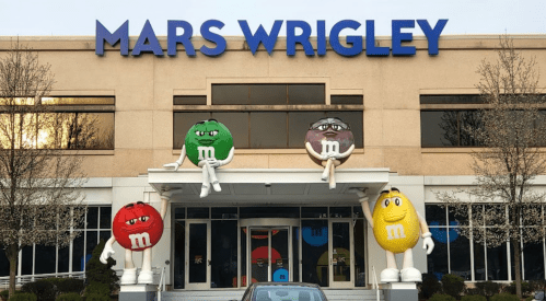 Exterior of the Mars Wrigley building, featuring large M&M character sculptures and a car in front.