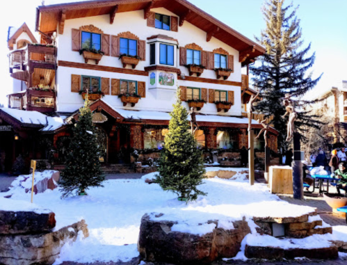 A charming chalet-style building with wooden shutters, surrounded by snow and evergreen trees.