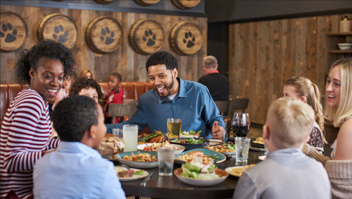 A diverse group of people enjoying a meal together at a restaurant, smiling and engaging in conversation.