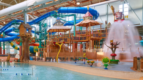 A vibrant indoor water park featuring slides, play structures, and a large splash area with water features.