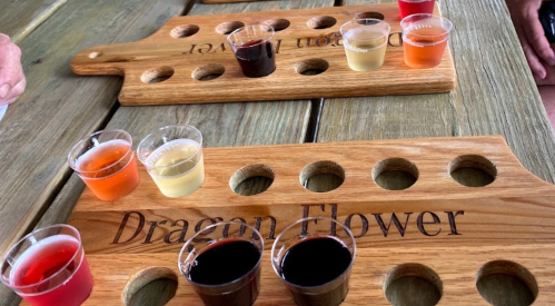 Two wooden tasting boards labeled "Dragon Flower" with small cups of various colorful drinks arranged on them.