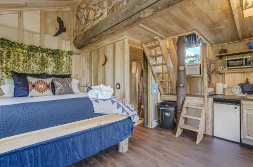 Cozy wooden cabin interior with a bed, kitchenette, and rustic decor, featuring natural elements and warm lighting.