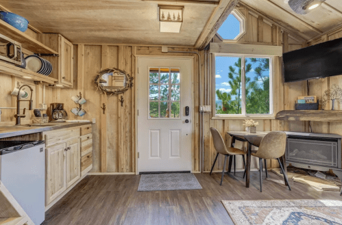 Cozy wooden interior of a small cabin with a kitchen, dining area, and large windows letting in natural light.