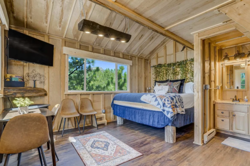 Cozy wooden cabin interior with a bed, seating area, and bathroom, featuring natural light and rustic decor.