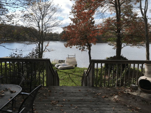 A serene lakeside view with autumn foliage, a wooden dock, and a calm water surface under a partly cloudy sky.