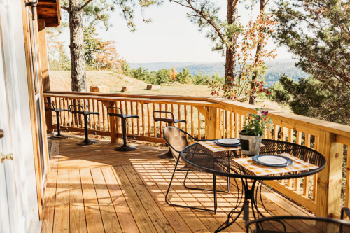 A wooden deck with a table and chairs, overlooking a scenic view of trees and hills in the background.