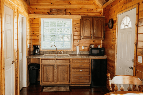 Cozy wooden kitchen with a sink, cabinets, a small fridge, and a window, featuring warm, rustic decor.