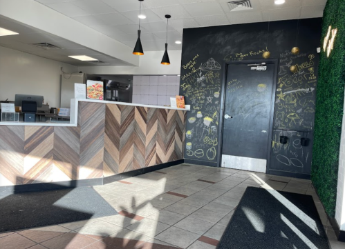 Interior of a restaurant featuring a wooden counter, chalkboard wall with drawings, and modern lighting.