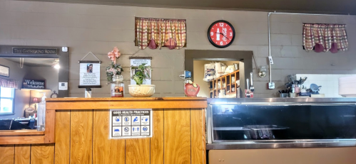 Interior of a cozy restaurant with wooden decor, a clock, and a counter displaying health practice guidelines.