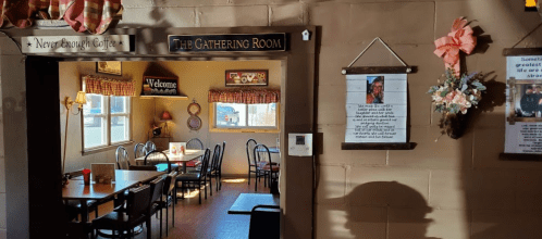 Cozy café interior with tables, chairs, and welcoming decor, featuring a sign for "The Gathering Room."