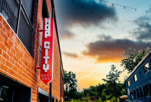 Sign for "Hop City" in West End, with a vibrant sunset and string lights in the background.
