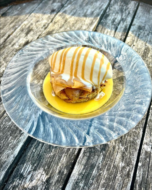 A dessert featuring a layered pastry with caramel drizzle, served on a glass plate over a yellow sauce.