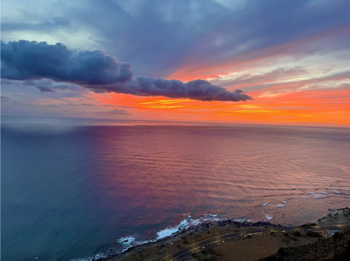 A vibrant sunset over the ocean, with colorful clouds reflecting on the water and waves gently crashing on the shore.
