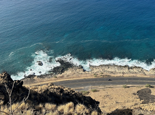 Aerial view of a coastal road winding along rocky shores with waves crashing against the rocks below.