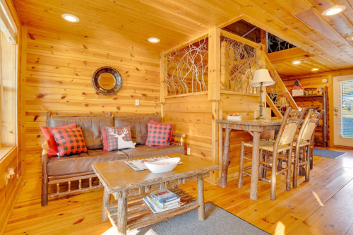 Cozy wooden interior of a cabin with a sofa, rustic table, and dining chairs, featuring warm lighting and natural decor.