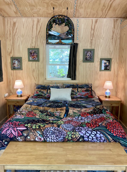 Cozy bedroom with a colorful floral bedspread, wooden furniture, and decorative wall art. Soft lighting from lamps.