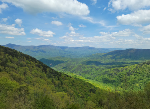 A panoramic view of lush green mountains under a bright blue sky with fluffy white clouds.