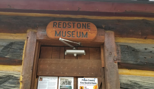 Sign above the entrance of the Redstone Museum, featuring rustic wooden beams and informational flyers below.