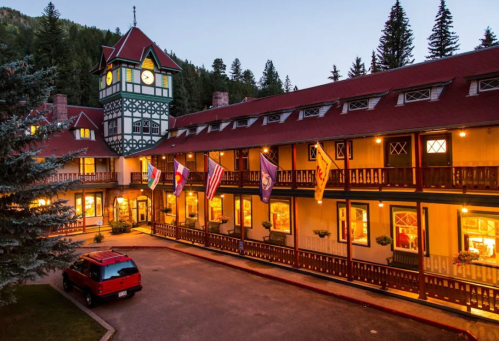 Historic lodge with a clock tower, surrounded by trees, featuring flags and warm lighting at dusk.