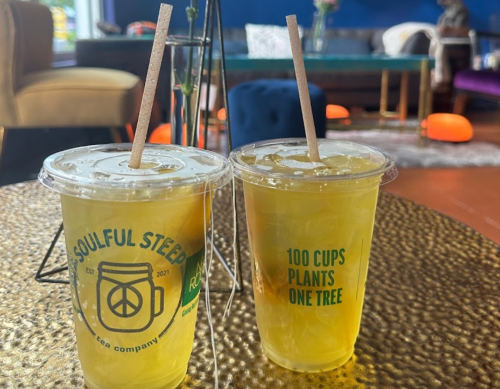 Two clear cups of iced tea with straws, labeled "Soulful Steeps" and "100 Cups Plants One Tree," on a textured table.