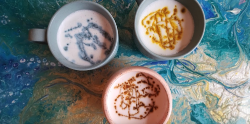 Three cups of coffee with artistic foam designs, placed on a colorful, marbled surface.