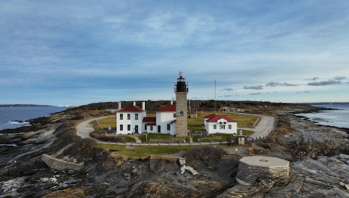 A scenic view of a lighthouse on a rocky shore, surrounded by green grass and water under a cloudy sky.