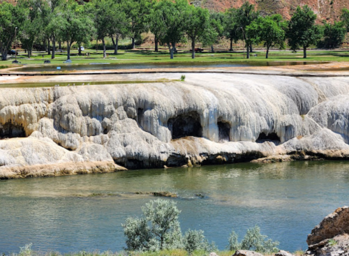 A rocky riverbank with mineral formations, surrounded by green trees and a calm water body.