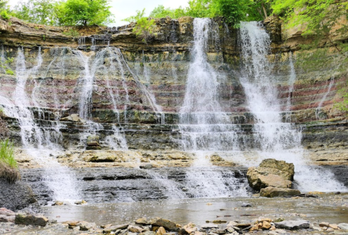 A scenic waterfall cascading over layered rock formations into a calm pool below, surrounded by lush greenery.