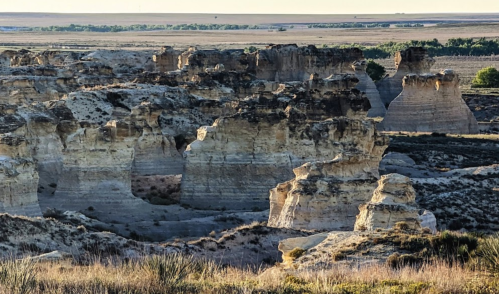 Rock formations rise from a rugged landscape, with grassy plains stretching into the distance under a clear sky.
