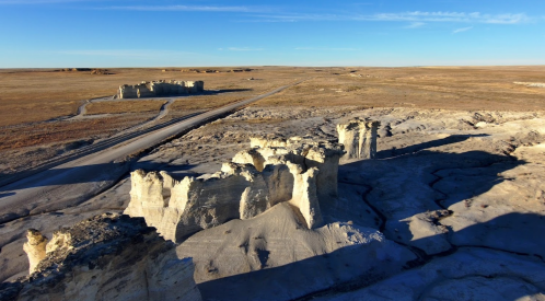 Aerial view of rugged rock formations and a winding dirt road in a vast, open landscape under a clear blue sky.