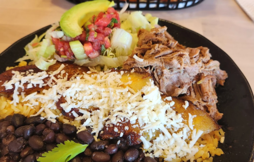 A plate of rice, black beans, shredded meat, fried plantains, lettuce, avocado, and salsa.