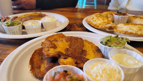 Plates of food featuring crispy tortillas, empanadas, and various dips like guacamole and sour cream on a wooden table.