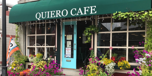 A charming café with a green awning, colorful flowers, and a welcoming entrance.