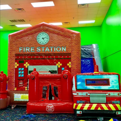 A colorful inflatable fire station play structure with a fire truck, set against a bright green wall.