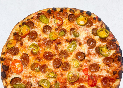 A round pizza topped with melted cheese, sliced tomatoes, and green and yellow peppers.