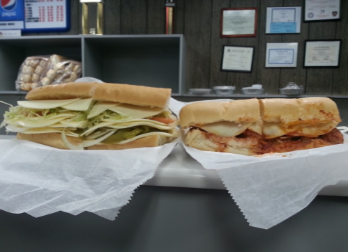 Two sandwiches on a counter: one with lettuce, tomato, and pickles; the other with sauce and melted cheese.