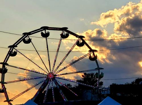 Silhouette of a Ferris wheel against a colorful sunset with clouds.