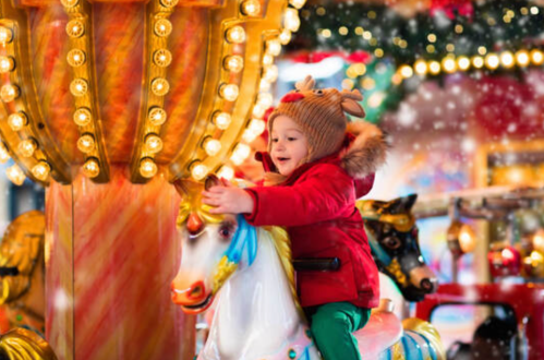 A joyful child in a red coat rides a colorful carousel horse, surrounded by festive lights and falling snow.