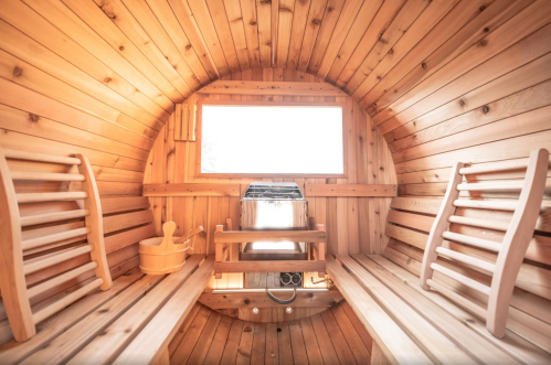 Interior of a wooden sauna with benches, a stove, and a window, creating a warm and inviting atmosphere.