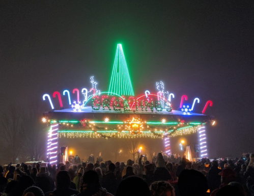 A festive pavilion adorned with colorful lights and decorations, surrounded by a crowd in a nighttime setting.