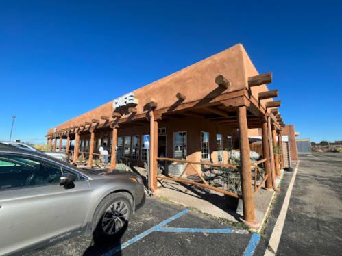 A southwestern-style café building with a wooden porch and clear blue sky in the background. Cars parked nearby.