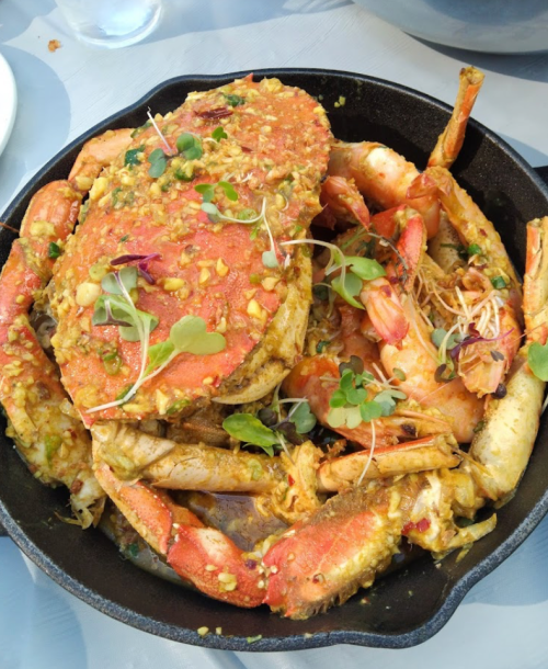 A cast iron skillet filled with a variety of crabs and shrimp, garnished with herbs and spices.