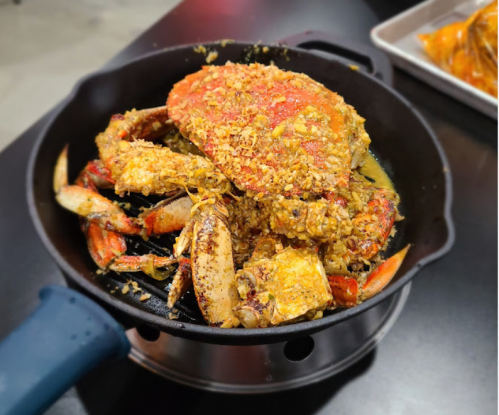 A cooked crab in a black pot, seasoned with spices and garnished, sitting on a table.