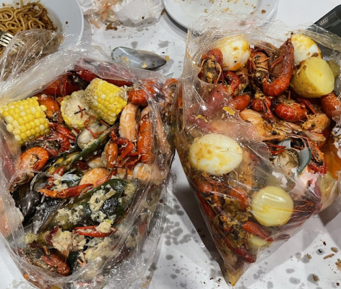 Two large bags filled with a variety of seafood, including shrimp, crab, corn, and potatoes, on a messy table.