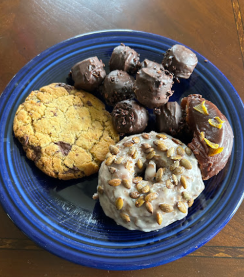 A blue plate with a chocolate chip cookie, chocolate-covered treats, and two donuts topped with seeds and icing.