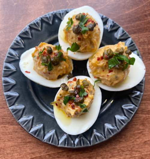 Four deviled eggs topped with capers and herbs on a decorative black plate.
