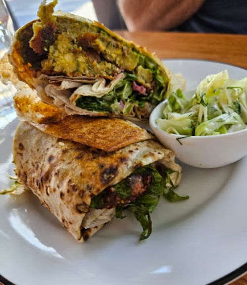 A close-up of a wrapped sandwich filled with greens and a side of coleslaw on a plate.