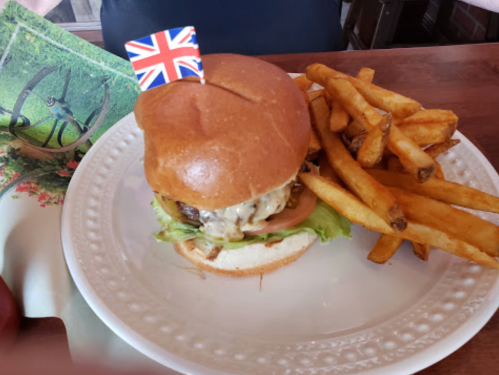 A burger with a British flag on top, served with a side of golden fries on a white plate.