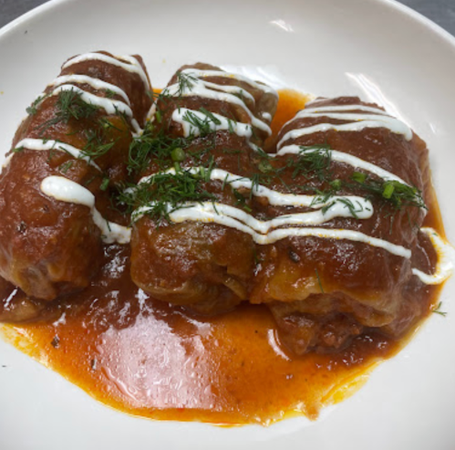 Three stuffed cabbage rolls drizzled with sour cream and garnished with herbs, served in a rich tomato sauce.
