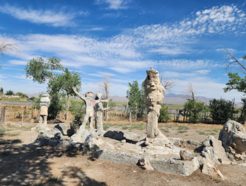 A weathered stone sculpture group in a grassy area, with trees and a blue sky in the background.